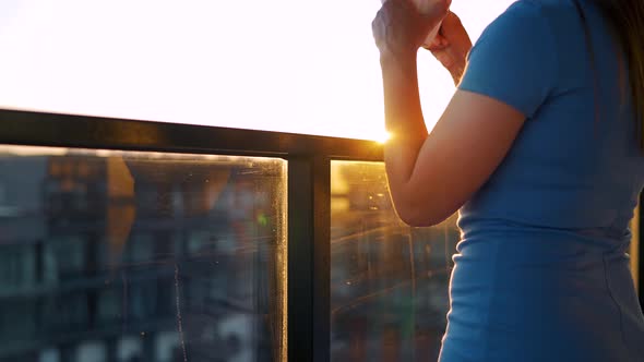 Woman with a Cup of Coffee Standing on the Balcony and Admire the Sunset