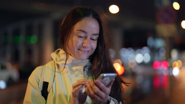 Happy Female City Dweller with Mobile Phone in Night City Street Sending Message By Smartphone