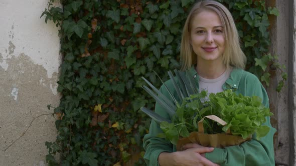 Smiling woman with vegetables in bag on ivy wall background