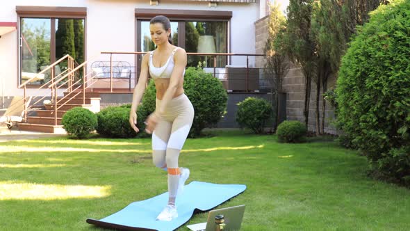 Fitness woman doing forward lunge exercises and watching online tutorials on laptop, training outdoo