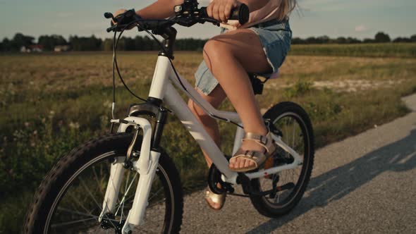 Tilt up of elementary age caucasian girl riding a bike bike at sunset time. Shot with RED helium cam