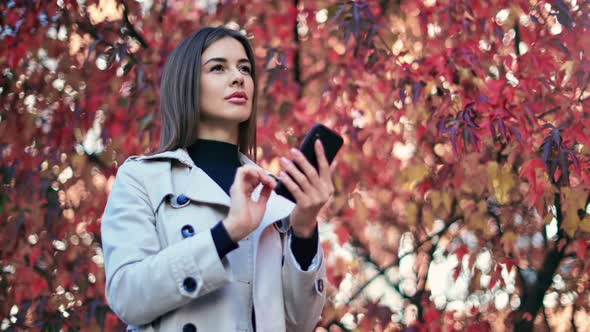 Joyful Young Woman Use Mobile Phone Standing Outdoor at Autumn Garden