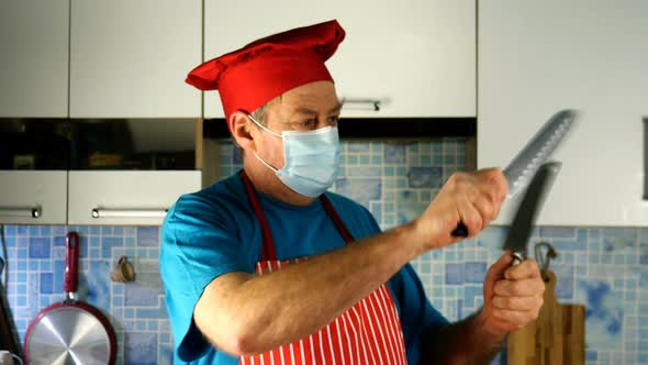 Senior Adult Cook Caucasian Ethnicity in Chefs Hat and Medical Mask Sharpens Knife on Knife