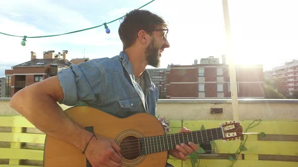 Handsome cheerful musician playing guitar at the rooftop party