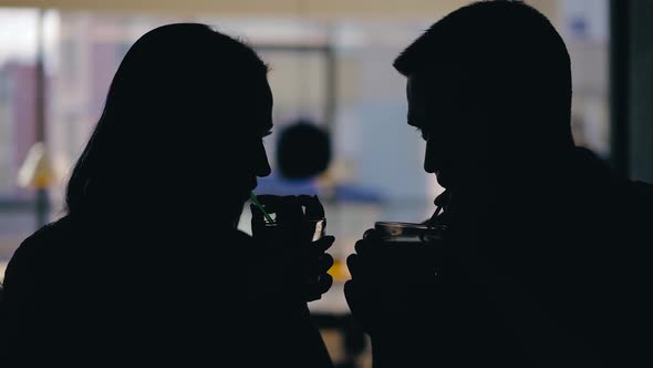 A man and a woman are drinking drinks from tubules on a blurred background in a cafe.