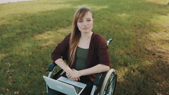 Serious Disabled Young Caucasian Woman in Wheelchair in the Park Stroking Her Hair on the Autumn