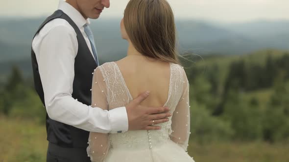 The Groom Strokes the Bride's Back Near Mountain Hills. Wedding Couple