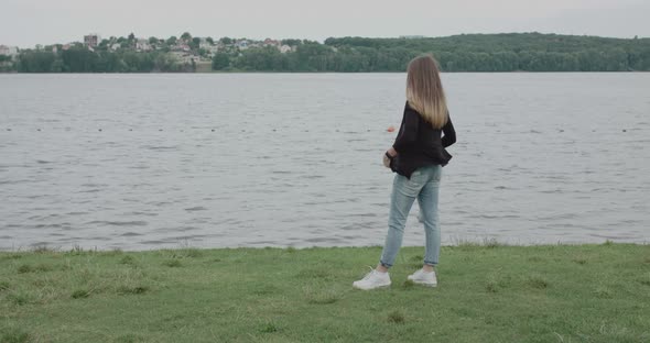 Back View of the Girl Stands at River in Windy Day and Corrects Her Cagdigan