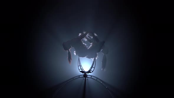 Girls Rotate in the Air While Sitting on a Hoop. Black Smoke Background. Silhouette