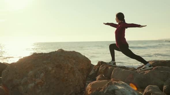 Woman doing asana warrior at wild beach. Back view. Tracking left. Slow motion.