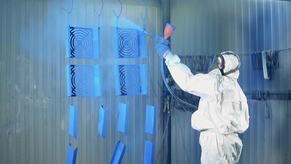 Blue Paint is Getting Sprayed Onto Metal Plates By a Female Worker