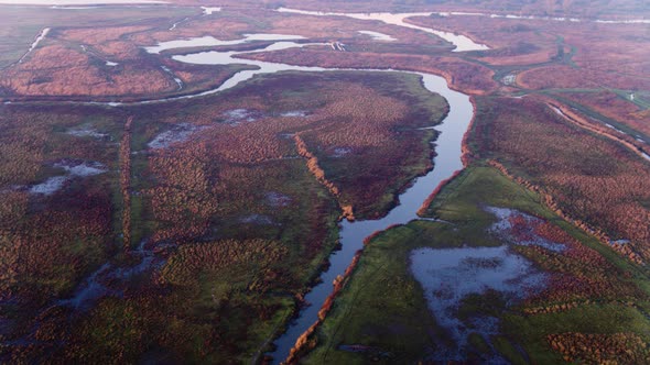 Scenic river delta through misty reddish reed and flooded farmlands; drone
