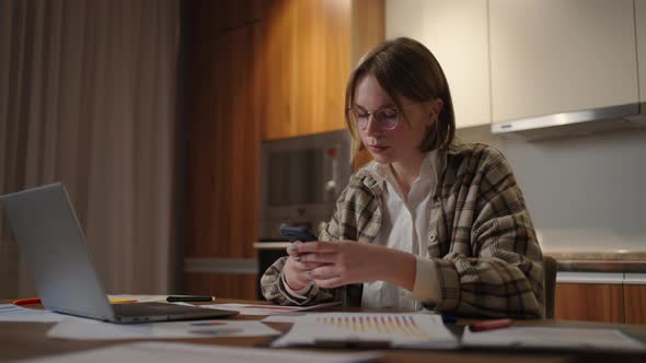 Happy Woman Using Mobile Phone While Working at Home with Laptop