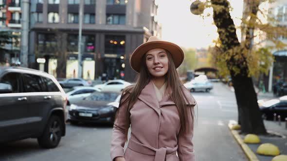 Charming young woman in a coat and hat walks down the street