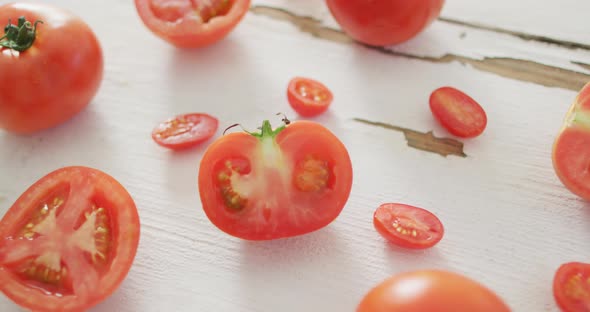 Video of fresh halved and whole red tomatoes on white rustic background