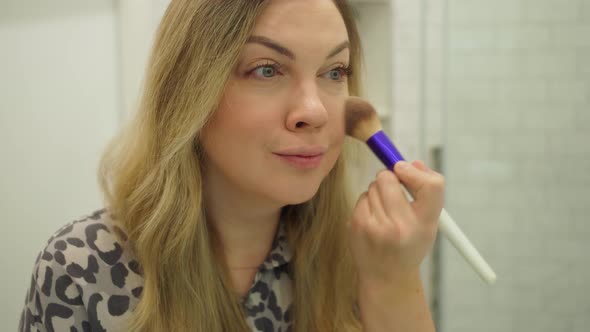 Beautiful Young Woman Doing Makeup with a Big Fluffy Brush in the Bath in Front of a Mirror Closeup