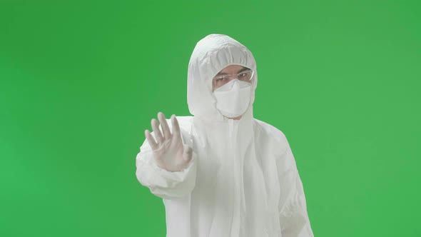 Asian Man Wear Protective Uniform PPE And Showing Hand Stop Sign In The Green Screen Studio