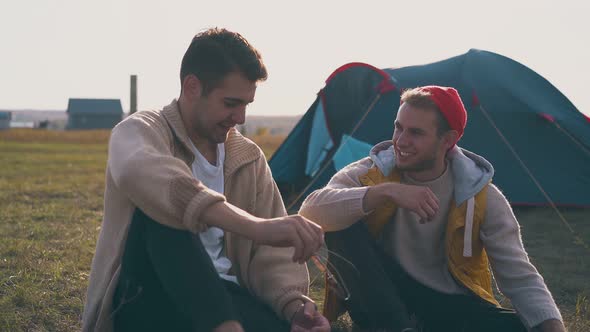 Smiling Men Talk Resting at Blue Tent in Camp on Meadow