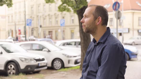 A Caucasian Man Smiles at the Camera in an Urban Area  a Colorful Street in the Blurry Background