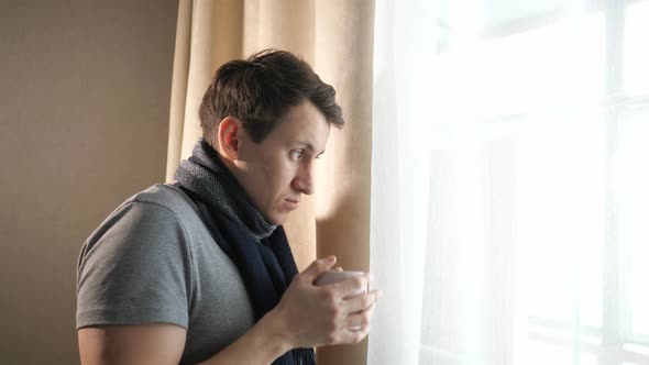 Sick Male with Mug Coughing Near Window