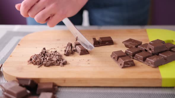 Woman Chopping Black Dark Chocolate on Wooden Cutting Board