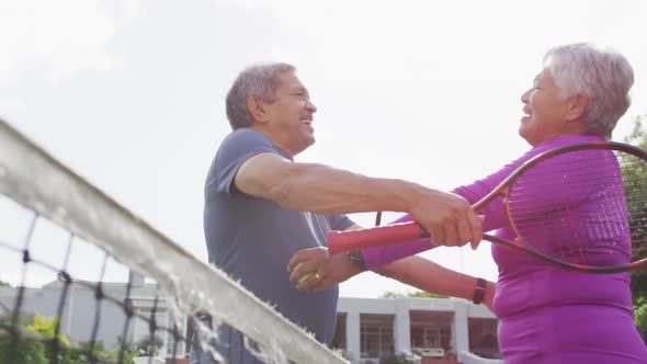 Video of happy biracial senior couple embracing on tennis court