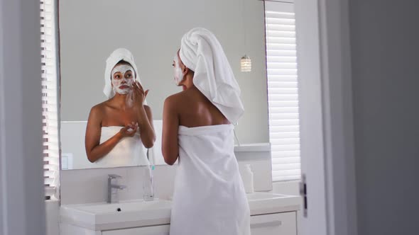 African american woman applying face mask while in the mirror at bathroom