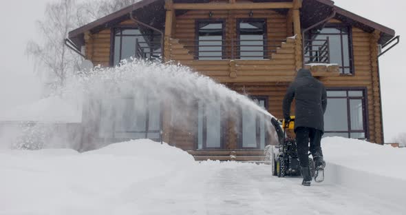 Man Removes Snow with Snowblower in Yard at Snowfall in Slow Motion