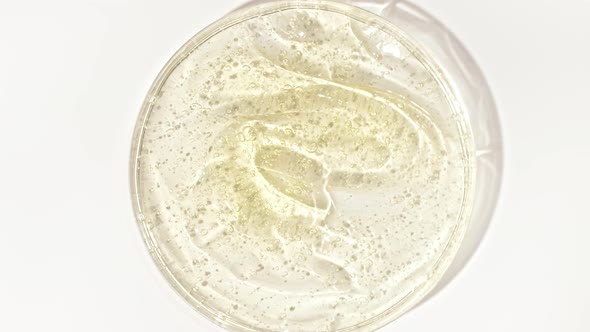 Rotation of Transparent Yellow Cosmetic Gel Fluid with Bubbles in a Glass Bowl of Petri alt