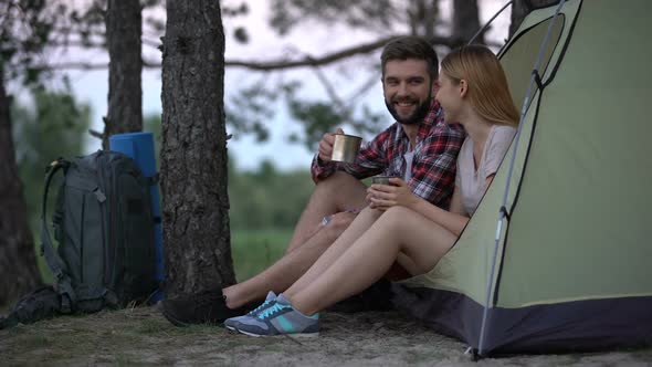 Young Couple Sitting in Tent Drinking Tea and Talking