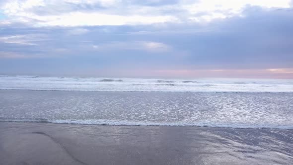 Aerial flying over the ocean towards the horizon with sunset clouds at beach