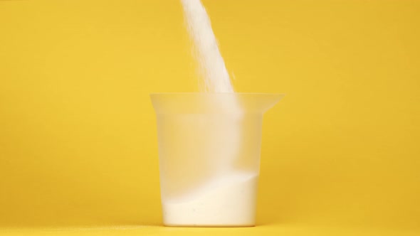 Pouring Detergent Powder Into Plastic Measuring Glass on Yellow Background Shooting of Detergent for