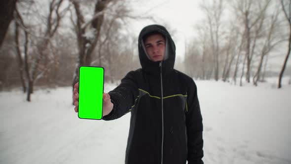 Man in Park Winter Shows Screen of Phone of Chomakey