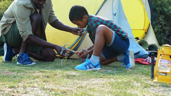 Father teaching son to use a hammer for setting up a tent