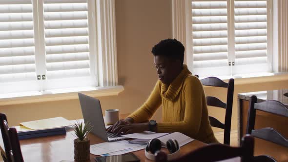 African american woman using laptop and reading documents while working from home