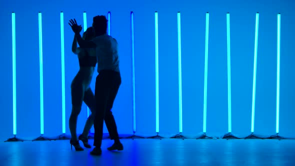 A Couple of Dancers Practice Salsa Dance Elements Against a Background of Bright Blue Neon Lights in