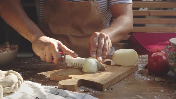 Men's Hands Cutting Onion on Wooden Board