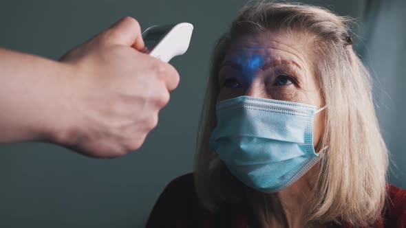 Digital Thermometer Measuring Body Temperature of an Elderly Woman with Medical Mask