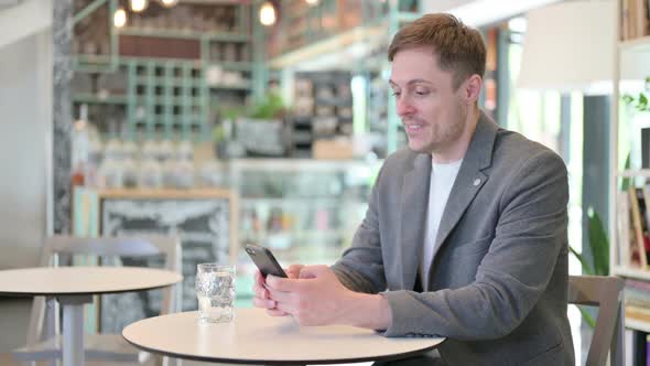 Young Man Celebrating Success on Smartphone in Cafe