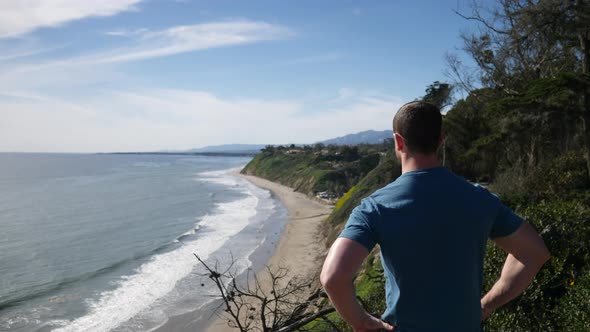 A fit, strong man standing on the edge of an ocean cliff lookout on a nature hiking trail with an ep