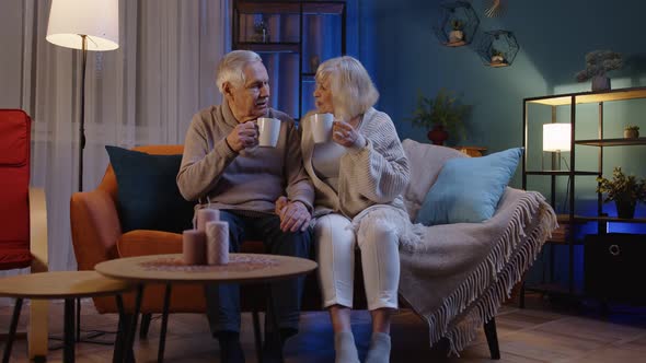 Carefree Mature Family Couple Relaxing on Sofa at Home Enjoying Conversation with Cups of Hot Tea