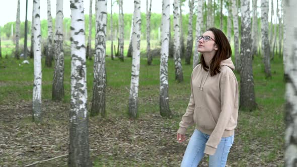 A Young Woman Walks Through a Birch Forest. A Girl Walks in the Park. View Through the Trees. 