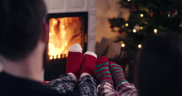 Couple feet in christmas woolen socks near fireplace with decorated tree in backg