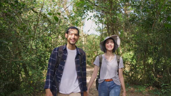 Young Asian man and woman friend or couple traveling  walking with happiness in the forest together.