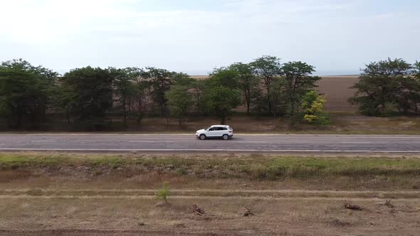 The Drone Follows a White Car Driving on a Road in a Steppe Area