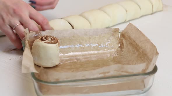 A Woman Puts Sliced Dough With Cinnamon Into A Baking Dish For Baking Cinnabons. Close Up Shot.