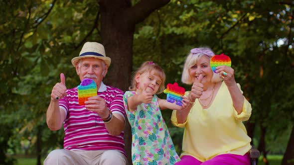 Senior Grandmother Grandfather with Granddaughter Holding Antistress Pop It Toy Games in Park