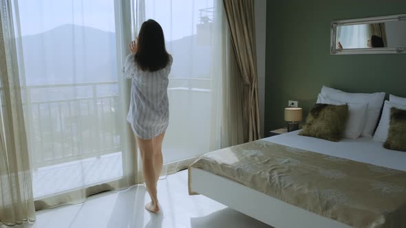 Close up back view Young brunette woman opening curtain looking through window