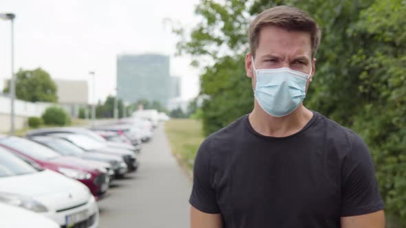 A Young Handsome Man in a Face Mask Acts Angry in a Parking Lot in an Urban Area