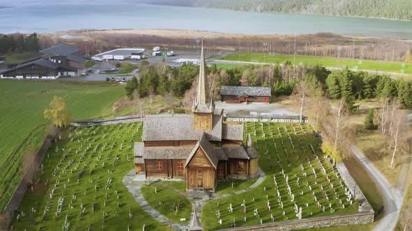 Tilt-Down Of Lom Stave Church With Cemetery In Green Meadows During Snowstorm In Norway. Aerial